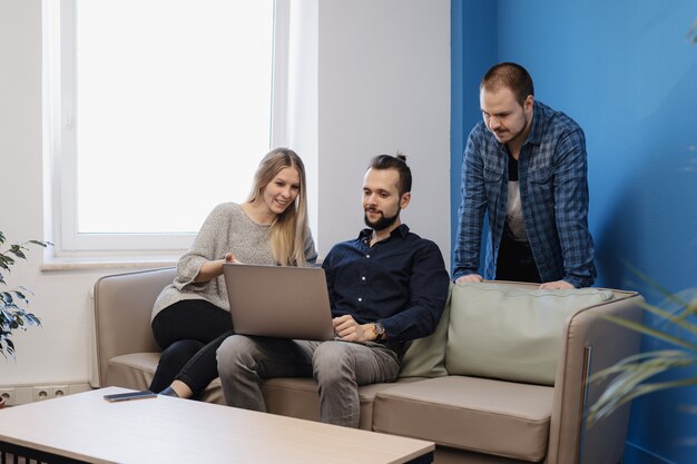 Команда из трех человек, работающих на ноутбуке в офисе на диване
