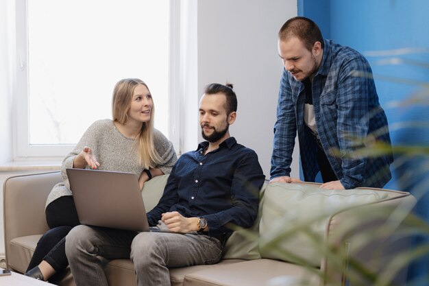 Team of three people working on laptop in the office on the sofa