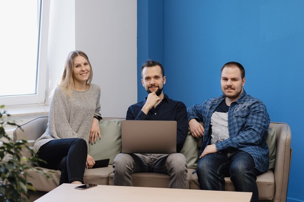 Team of three people working on laptop in the office on the sofa