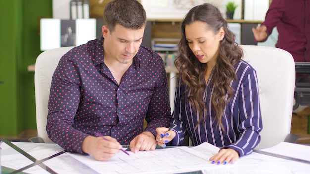 Team of two architects discussing over blue prints in cozy office interior