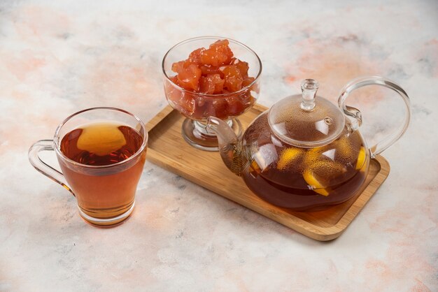 Teapot of black tea and quince jam on wooden plate. 