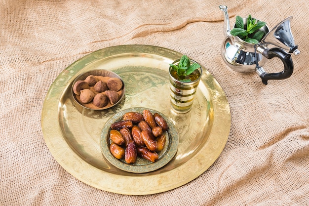 Teapot near mug with plant twigs, dried fruits and chocolate sweets on tray