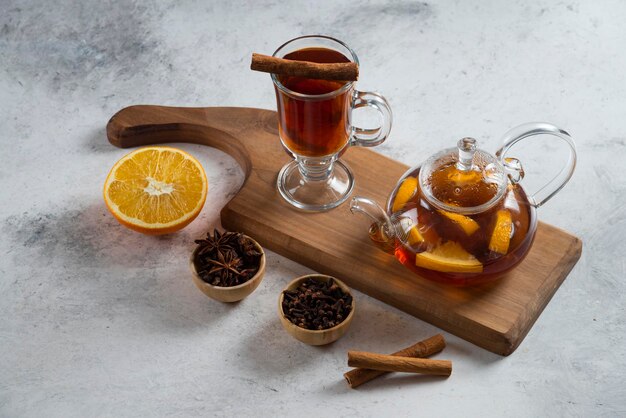 A teapot with tea and slice of orange on wooden board.