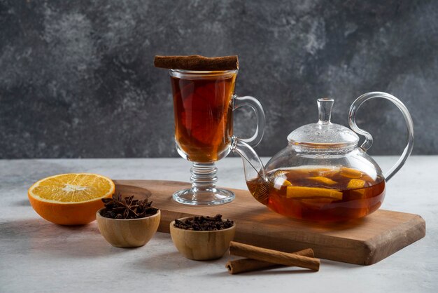 A teapot with tea and slice of orange on wooden board.