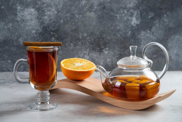 A teapot with tea and slice of orange on wooden board.