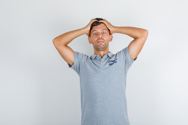Technical service man in grey t-shirt holding head with hands and looking tired