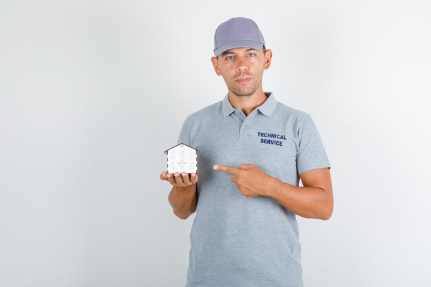 손가락으로 집 모델을 보여주는 모자와 회색 티셔츠에 기술 서비스 남자