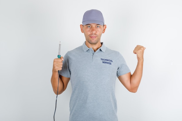 Free photo technical service man holding screwdriver and pointing backwards in grey t-shirt with cap