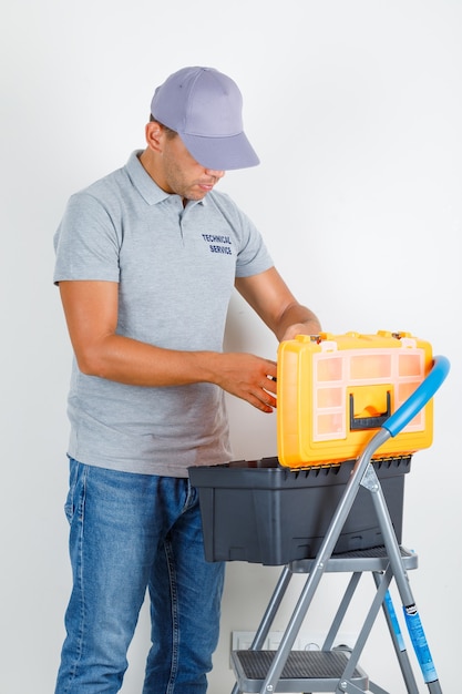 Foto gratuita uomo di servizio tecnico che esamina la cassetta degli attrezzi in maglietta grigia con cappuccio e che sembra occupato