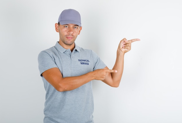 テクニカルサービスの男性がキャップ付きのグレーのTシャツに指を向けてポジティブに見える