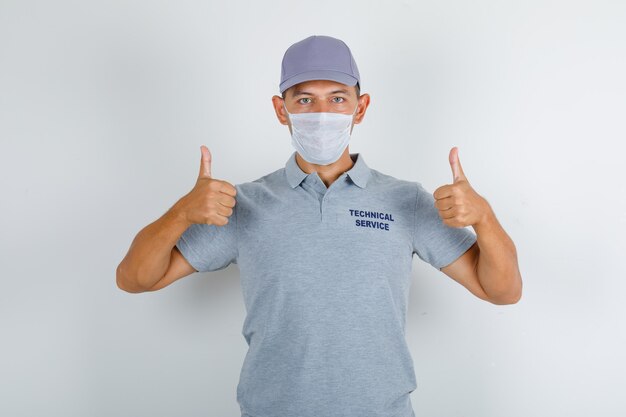 テクニカルサービスの男性がキャップと医療マスク付きのグレーのtシャツに親指を表示して慎重に見て