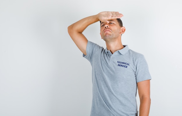 Человек технической службы, стоящий с рукой на лбу в серой футболке и разочарованный
