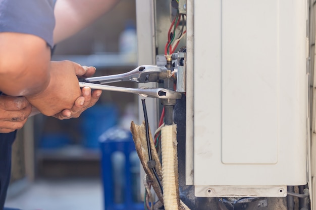 Technician man using a wrench fixing modern air conditioning system, maintenance and repair concept