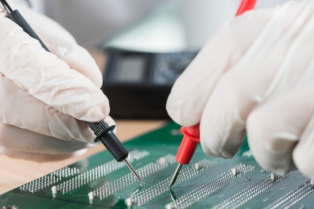 Free photo technician wearing gloves examining computer circuit board with digital multimeter