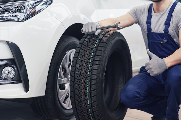 Technician with a blue workwear, holding a wrench and a tire while showing thumb up