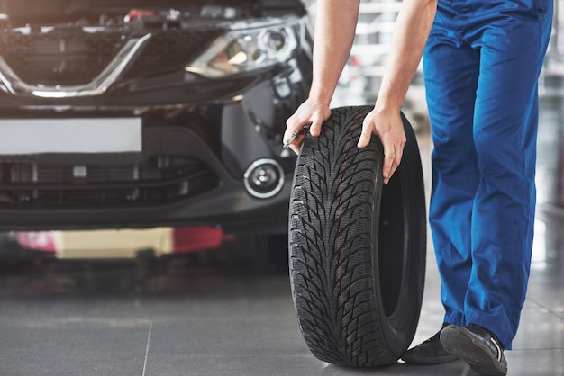 Technician with a blue workwear, holding a wrench and a tire while showing thumb up.