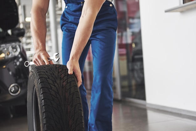 Technician with a blue workwear, holding a wrench and a tire while showing thumb up.