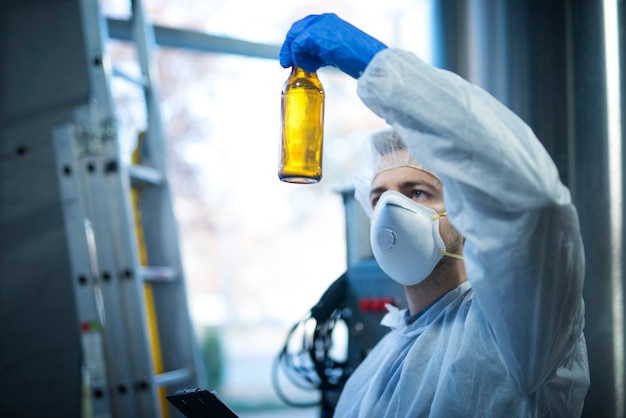 Эксперт-технолог на заводе по производству пива держит стеклянную бутылку и проверяет качество