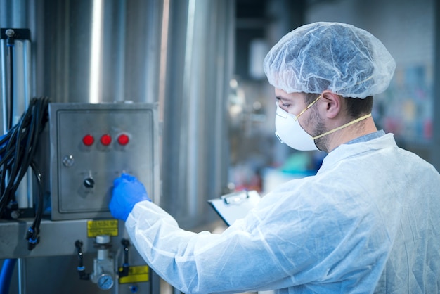 Foto gratuita tecnologo in uniforme protettiva operante macchina industriale nella linea di produzione in fabbrica