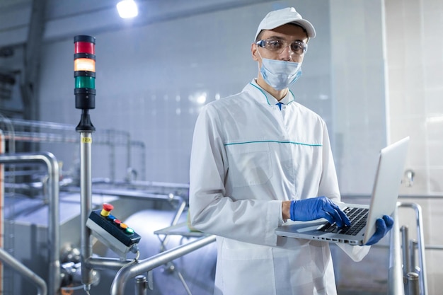 Technologist in a white coat with a laptop in his hands controls the production process in the dairy shop Place for writing Technologist with a laptop computer is at the factory