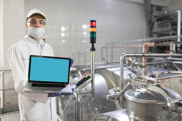 Free photo technologist in a white coat with a laptop in his hands controls the production process in the dairy shop place for writing technologist with a laptop computer is at the factory