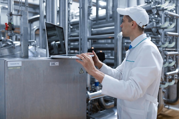 Technologist in a white coat with a laptop in his hands controls the production process in the dairy shop Quality control at the dairy plant