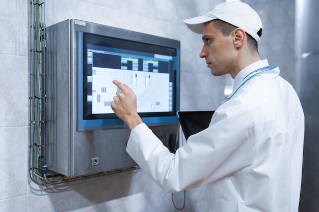 Technologist in a white coat with a laptop in his hands controls the production process on a digital screen in the dairy shop Quality control at the dairy plant