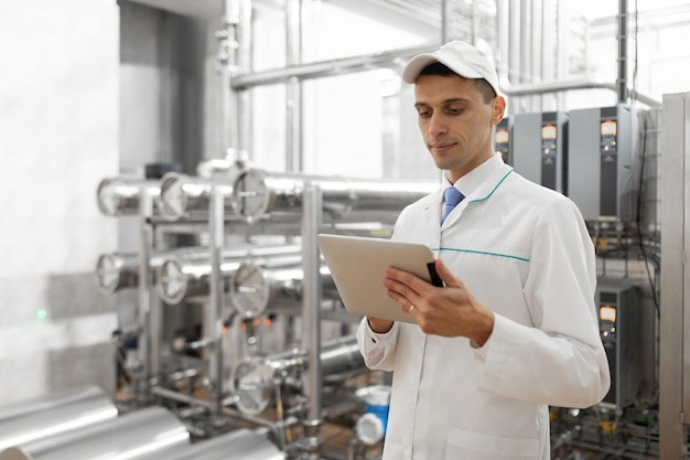 Technologist in a white coat with a tablet in his hands controls the production process in the dairy shop Quality control at the dairy plant