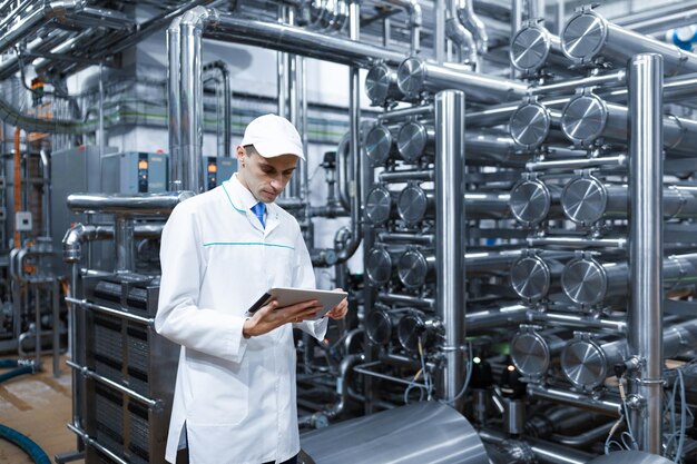 Technologist in a white coat with a tablet in his hands controls the production process in the dairy shop Quality control at the dairy plant