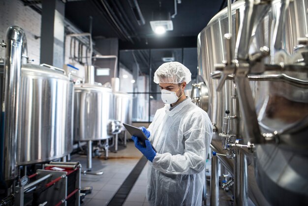 Technologist in white protective clothes checking production on his tablet