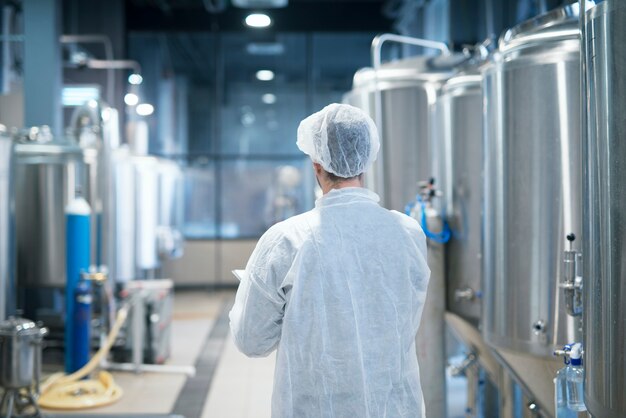 Технолог в белом защитном костюме идет по производственной линии пищевой фабрики, проверяя качество