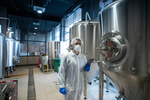 Technologist in white protective uniform holding tablet and controlling food production in processing factory