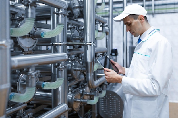 Technologist with grey tablet in his hands make a set up of the production line while standing at the department of dairy factory