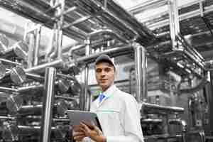 Free photo technologist with grey tablet in his hands make a set up of the production line while standing at the department of dairy factory