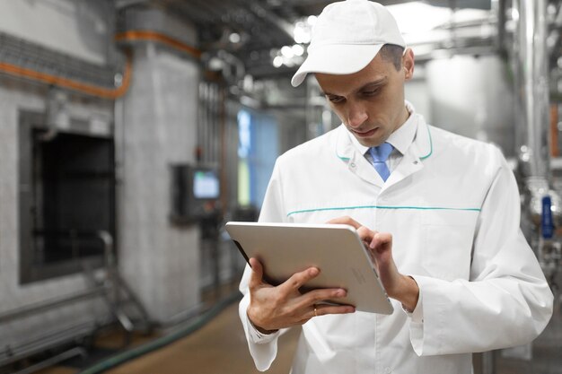 Technologist with grey tablet in his hands make a set up of the production line while standing at the department of dairy factory