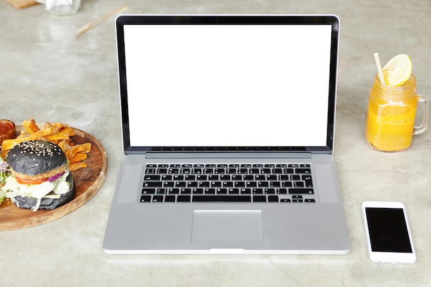 Free photo technology, business and working process. front view of workspace of freelancer: open laptop computer with copy space for your design, resting on table with smart phone