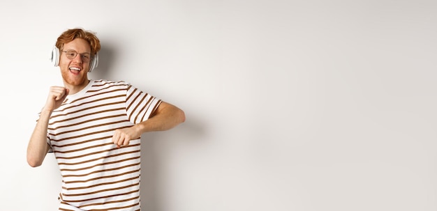 Free photo technology concept happy redhead man listening music in headphones and dancing cheerful standing in