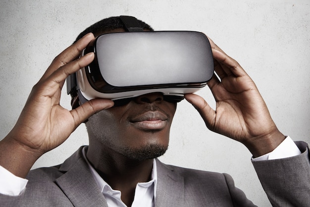 Technology and entertainment. Successful dark-skinned office worker in elegant gray suit experiencing virtual reality using VR headset glasses. 