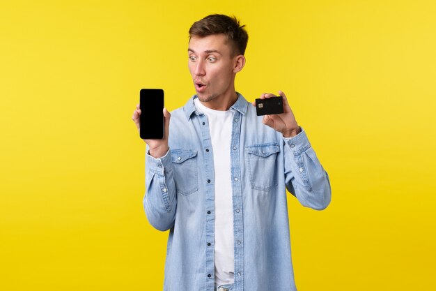기술, 라이프 스타일 및 광고 개념입니다. 감동하고 놀란 금발 남자는 휴대폰 화면을 보고 스마트폰 디스플레이와 신용 카드를 보여주며 주문을 하는 것처럼 와우라고 말합니다.