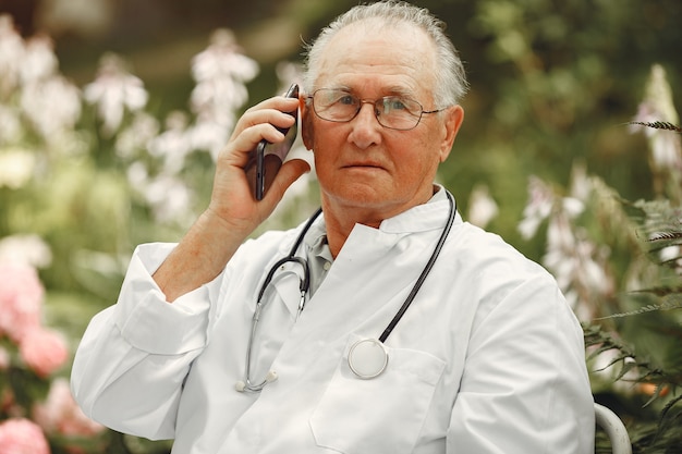 Technology, people and communication concept. Senior man at summer park. Doctor using a phone.