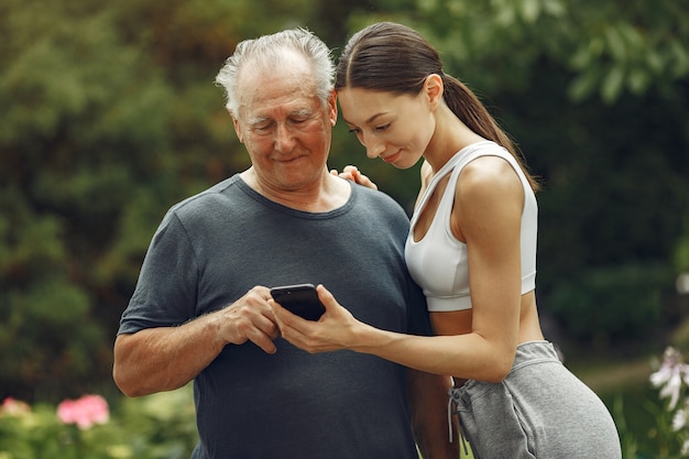 Technology, people and communication concept. Senior man at summer park. Grangfather with granddaughter.