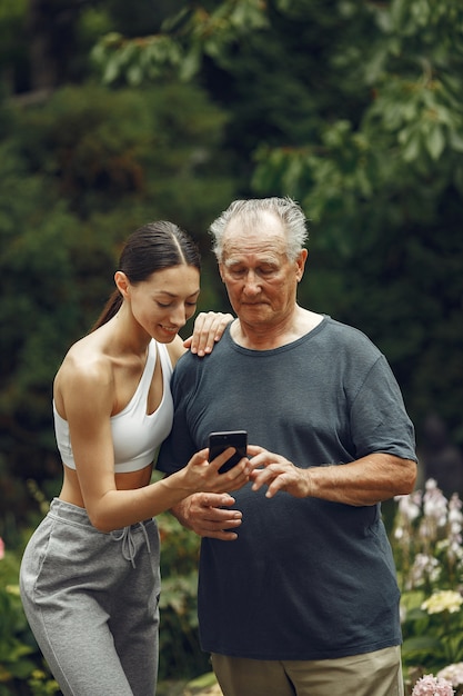 Technology, people and communication concept. Senior man at summer park. Grangfather with granddaughter.