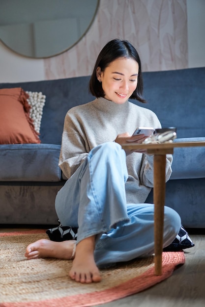 免费照片技术和人年轻时尚的亚洲女人坐在家里与她的智能手机短信usi