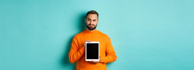 Technology skeptical and displeased guy showing digital tablet screen frowning disappointed standing