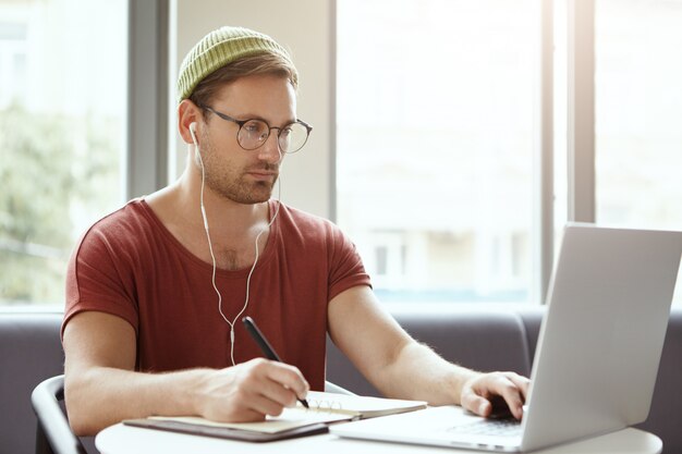 Technology, work and job concept. Successful male translator works remotely, writes in notebook with pen