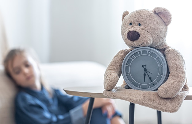 Teddy bear with an alarm clock on a blurred background of a little girl's room.