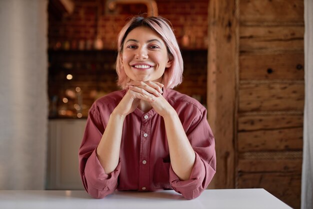 Teen age, youth, style and self expression concept. Portrait of positive happy teenage girl with bob pinkish hairstyle and facial piercing relaxing indoors