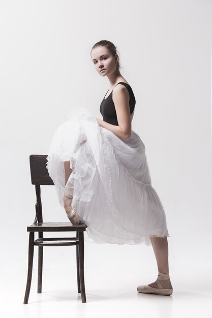 Молодая балерина в белой юбке позирует возле стула