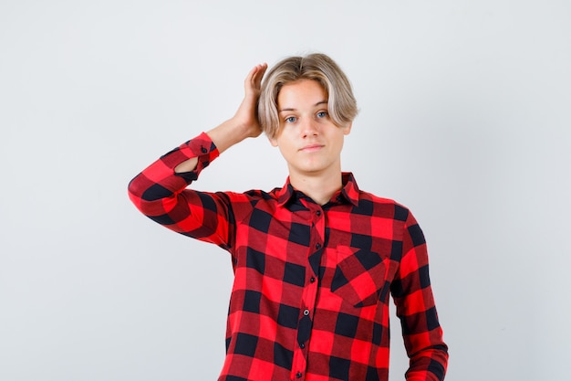 Teen blond male with hand near head in casual shirt and looking thoughtful. front view.