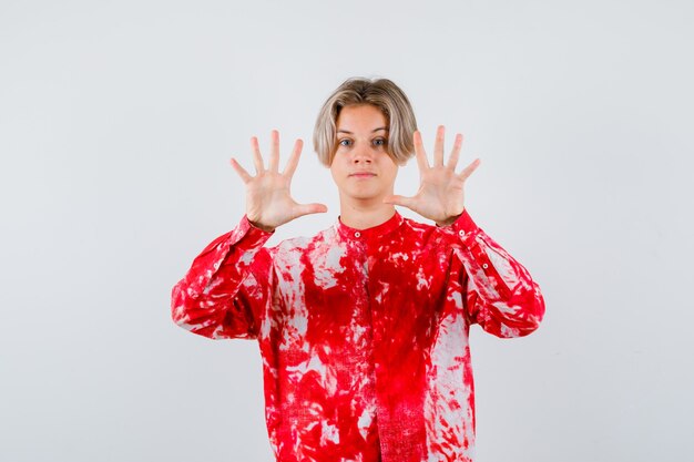 Teen blonde male in oversize shirt showing surrender gesture and looking cheerless , front view.